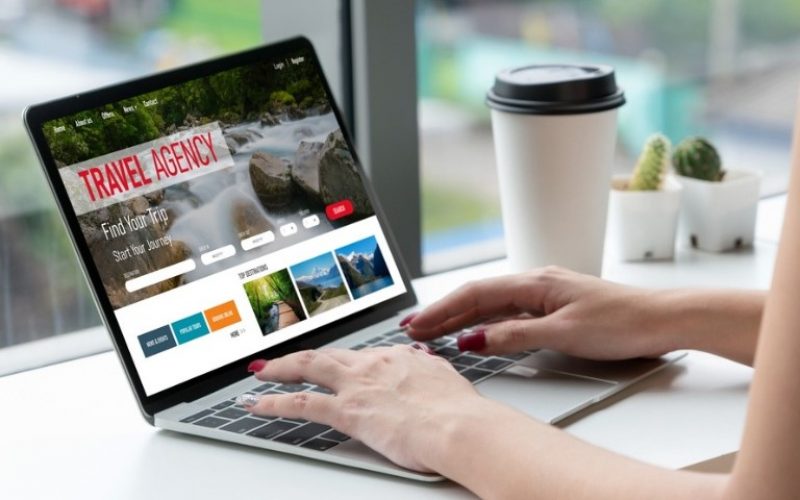 Hands typing on a laptop displaying a travel agency website with a waterfall background